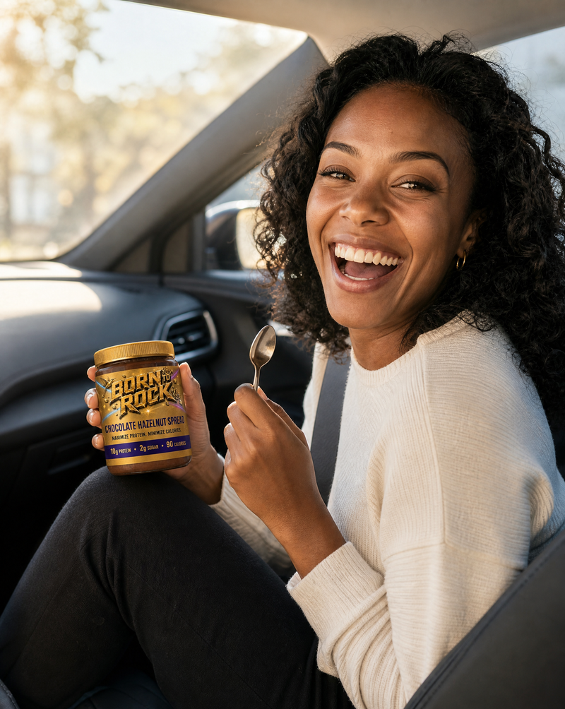 A woman laughing in the passenger seat of a parked car, holding the jar and a small spoon