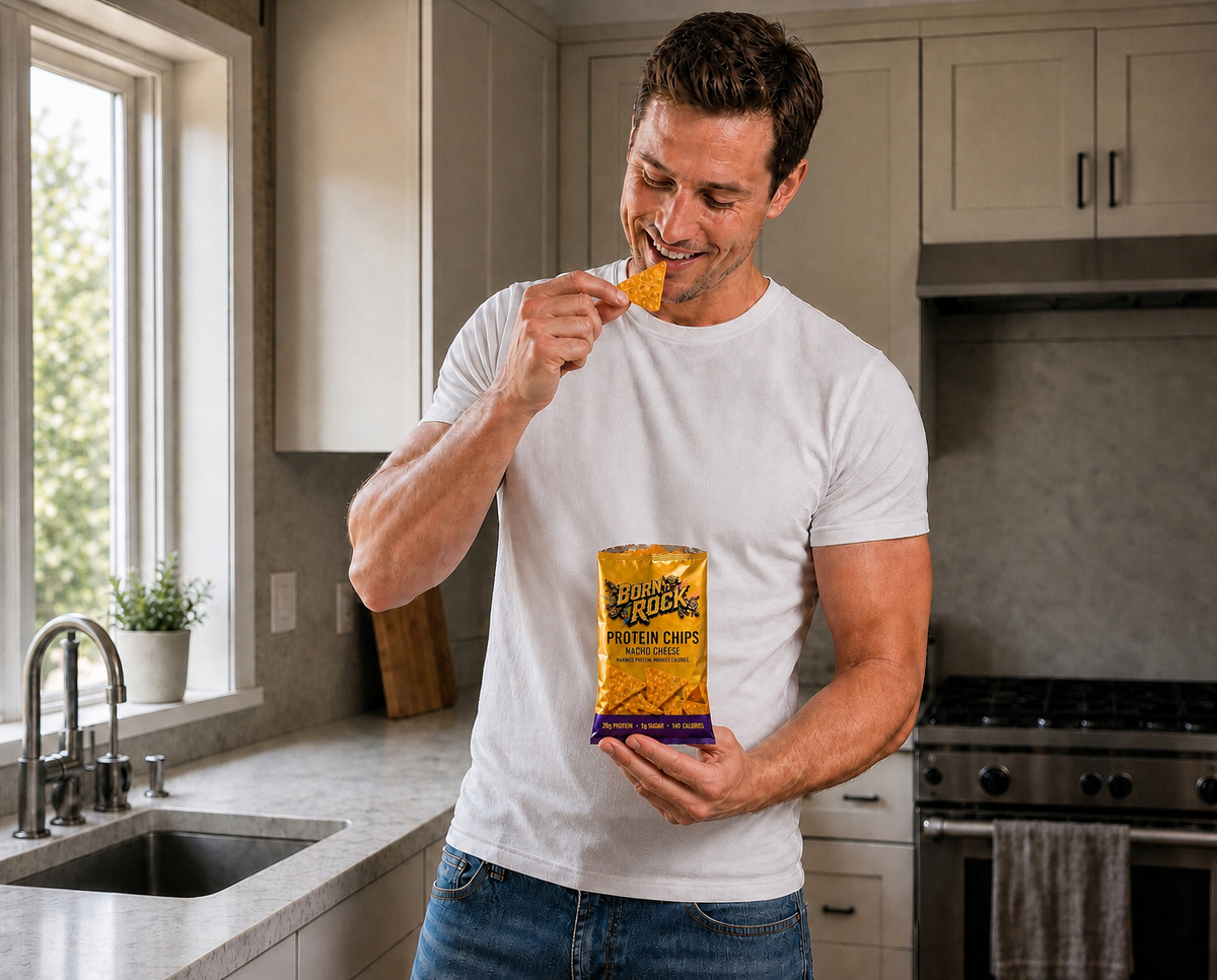 A man in a home kitchen holding the bag and raising a triangular nacho chip to his mouth