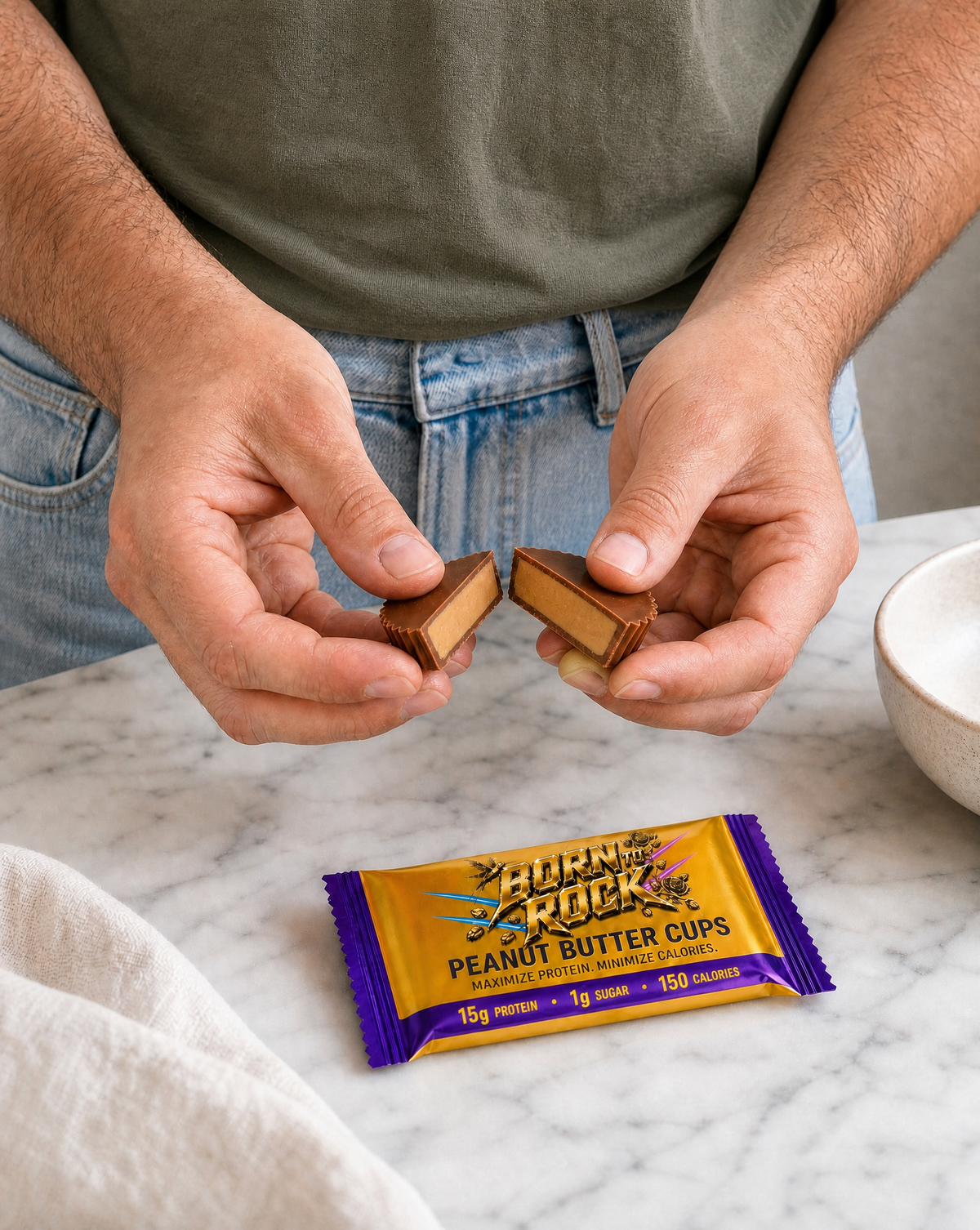 Two hands snapping a peanut butter cup in half to show the smooth creamy filling, the wrapped pack on the marble counter below